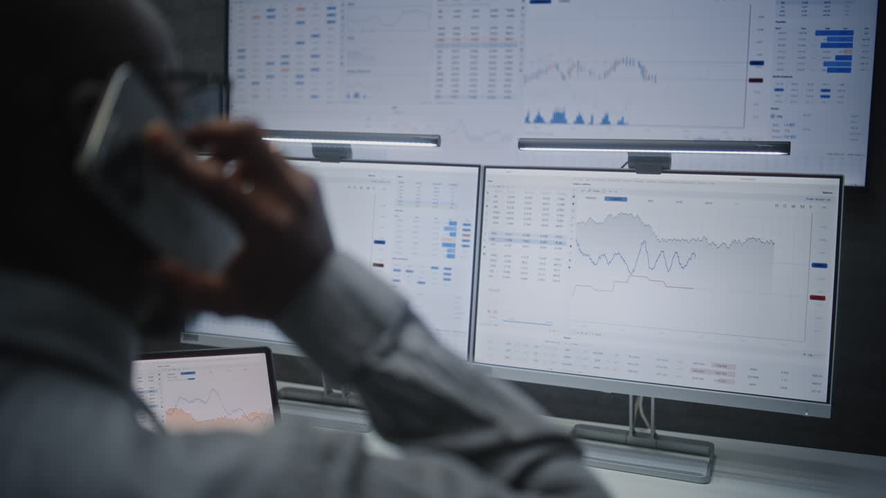 Person on phone looking at multiple stock market monitors