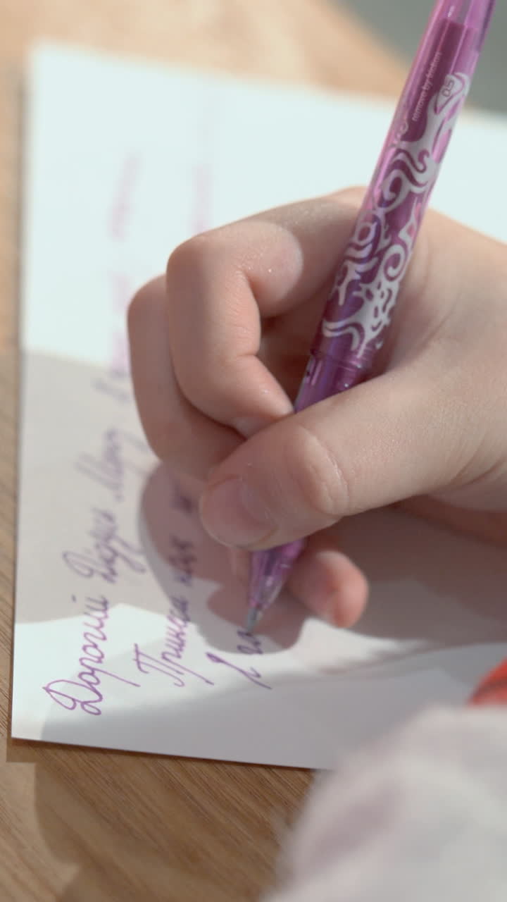 Close-up of children's hands. The girl writes a letter with a pen on paper in Ukrainian. Vertical video
