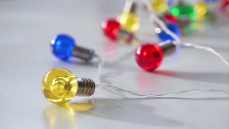 Brightly-colored-Christmas-LED-bulbs—blue,-red,-yellow,-and-green—are-spread-out-on-a-white-surface