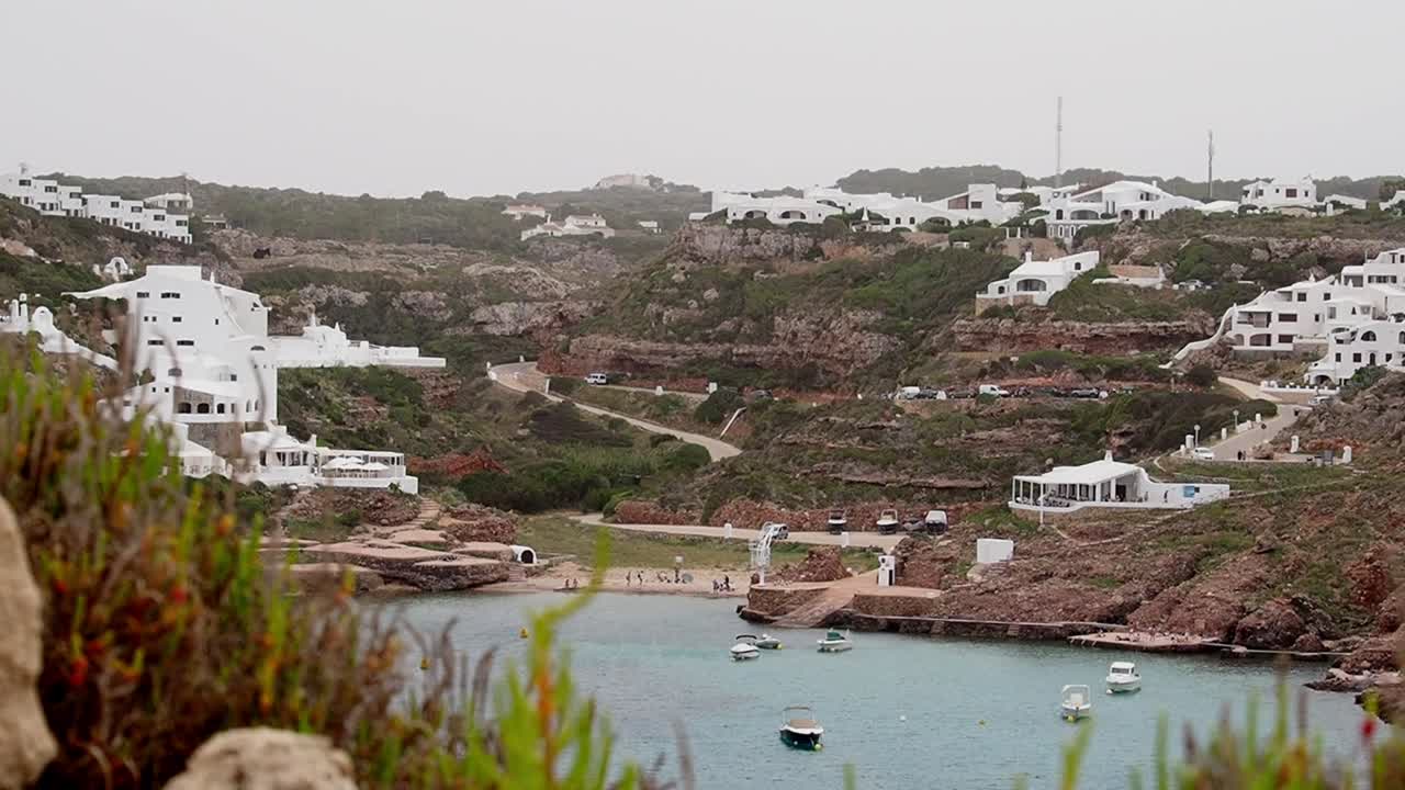 Cala Morell panoramic view with coastal houses, crystal-clear water, and boats
