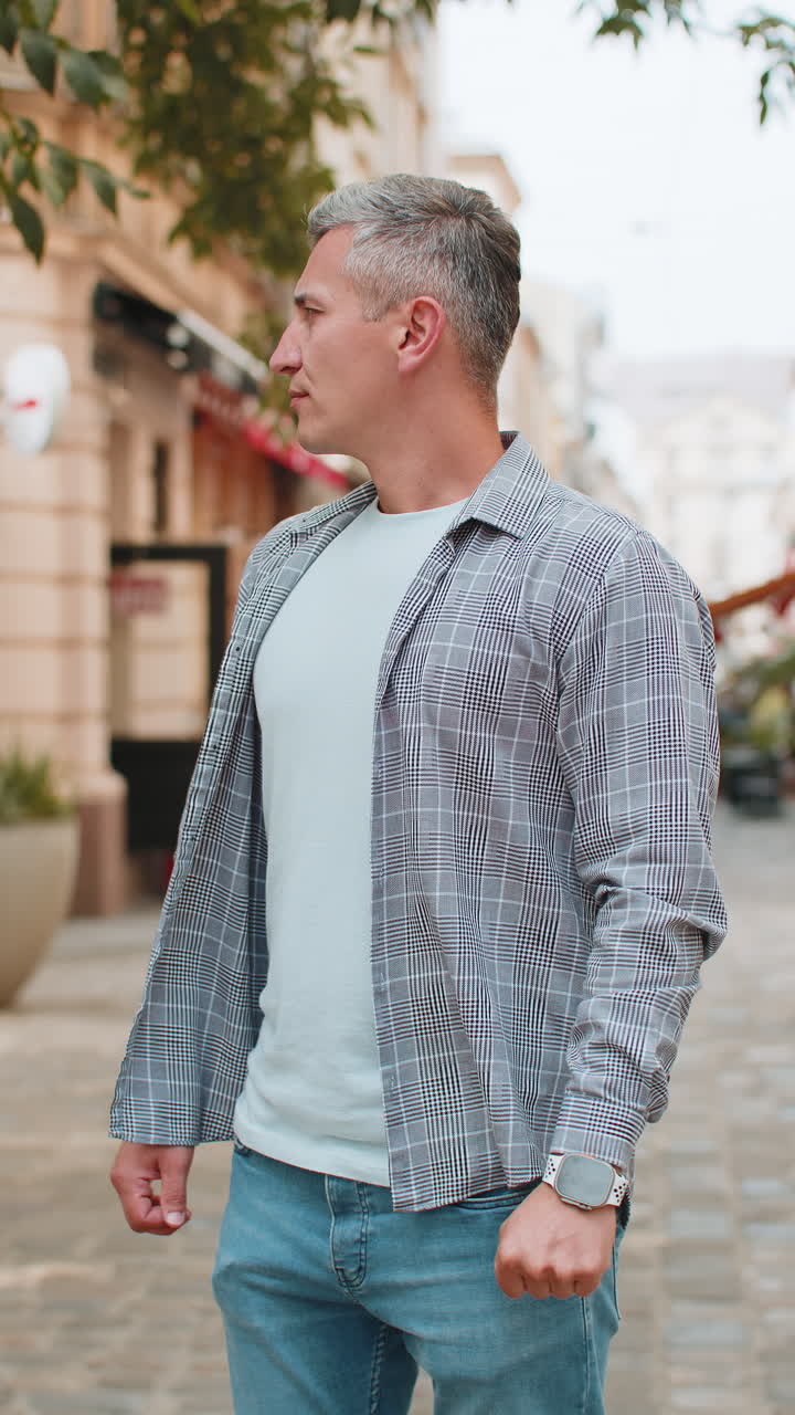 Mature man looking at wristwatch while waiting for someone feeling upset about being late in city