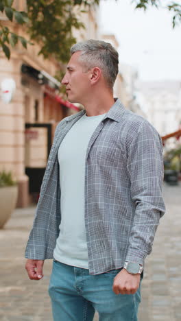 mature man looking at wristwatch while waiting for someone feeling upset about being late in city