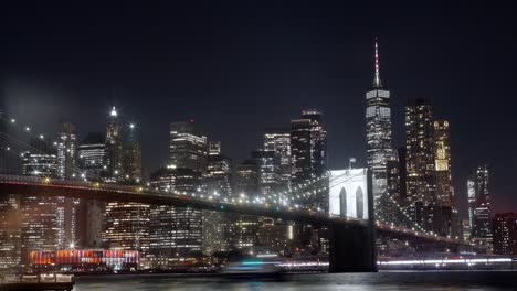 wide panoramic timelapse view of the brooklyn bridge and manhattan at night, boats passing by in the east river.