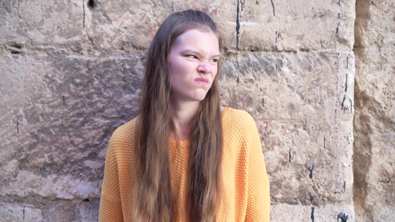 Una giovane donna posa con grazia con un accogliente maglione giallo davanti a un muro di pietra rustico.