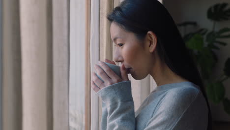 아름다운 아시아 여성이 창문 밖을 바라보고 커피를 마시고 신선한 새로운 날을 즐기며 휴식을 취하고 있습니다.