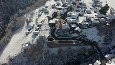 drone flying away from church and revealing a beautiful small mountain town in winter