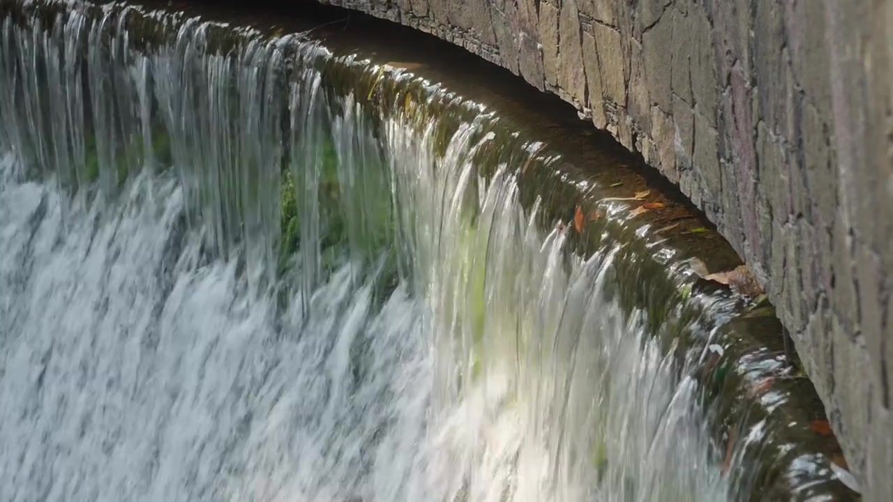 Sfioratore in pietra curvo con acqua dolce a cascata che scorre su una parete strutturata