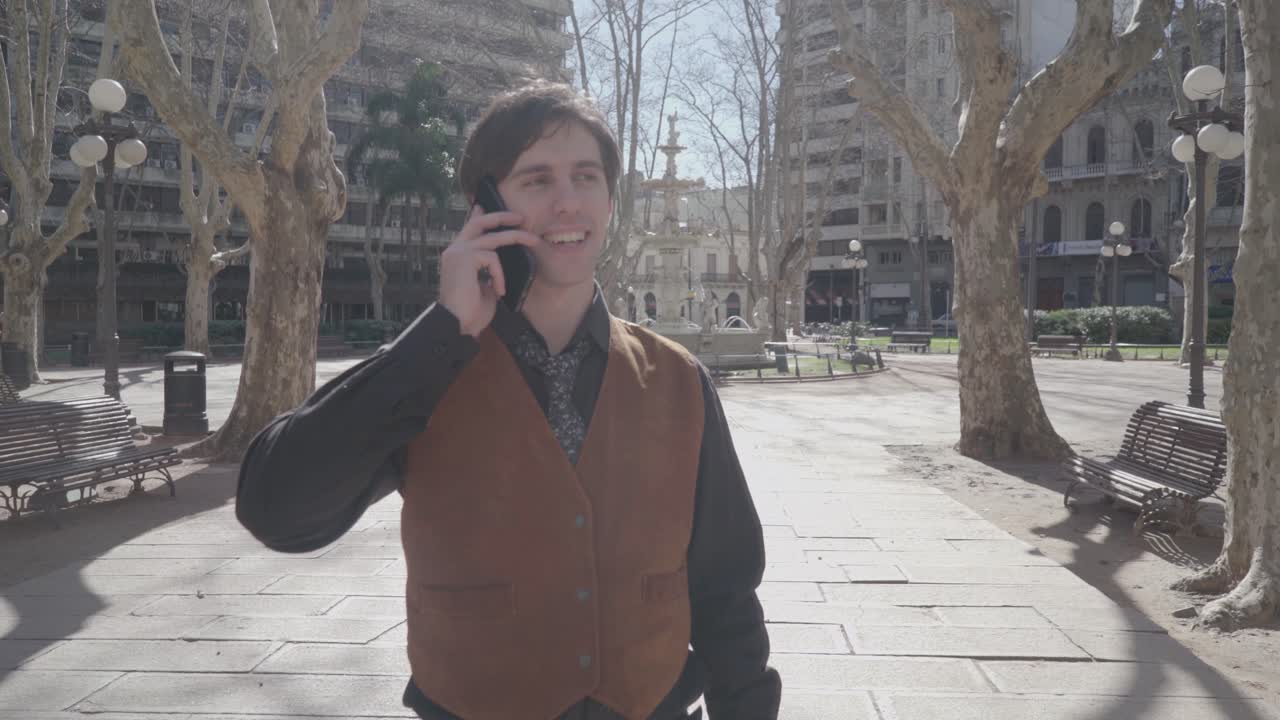 Young man in shirt and tie speaks on cellphone and laughs cheerfully