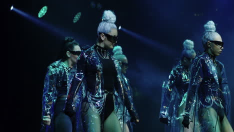 a group of women dance on stage with a blue backdrop