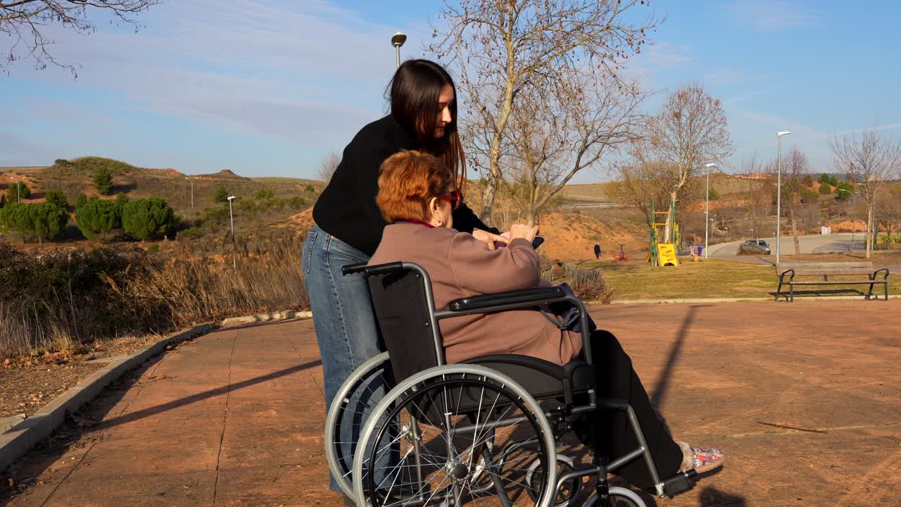 Granddaughter taking selfie with grandmother in wheelchair on sunny day