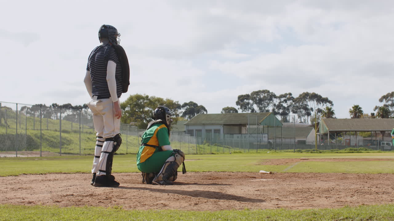 Giocatrici di baseball multietniche e arbitro uomo che battono la palla e corrono su un campo da gioco.
