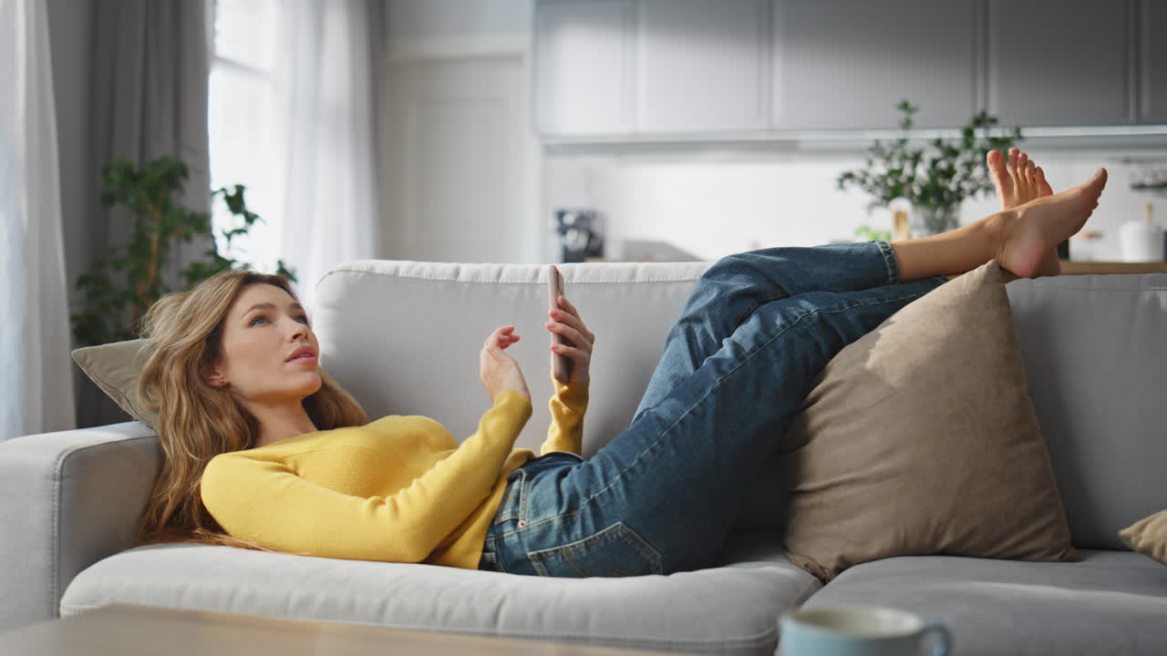 Relaxed woman browsing smartphone chilling couch at home. Lady creating message
