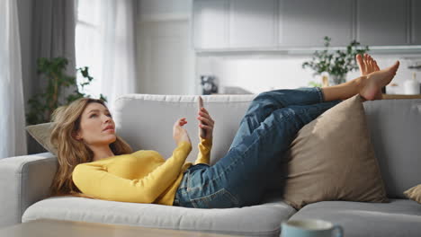 relaxed woman browsing smartphone chilling couch at home. lady creating message