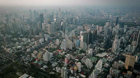 aerial scenic drone footage of the skyline of downtown bangkok, thailand covered in smog during sunset during the smokey burning season