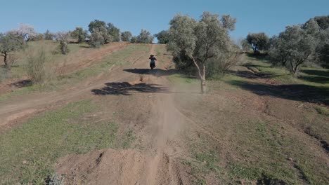 aerial tracking dolly shot of a driving motocross on a motocross track in malaga spain with dusty track, trees and hills on a cloudless sunny day