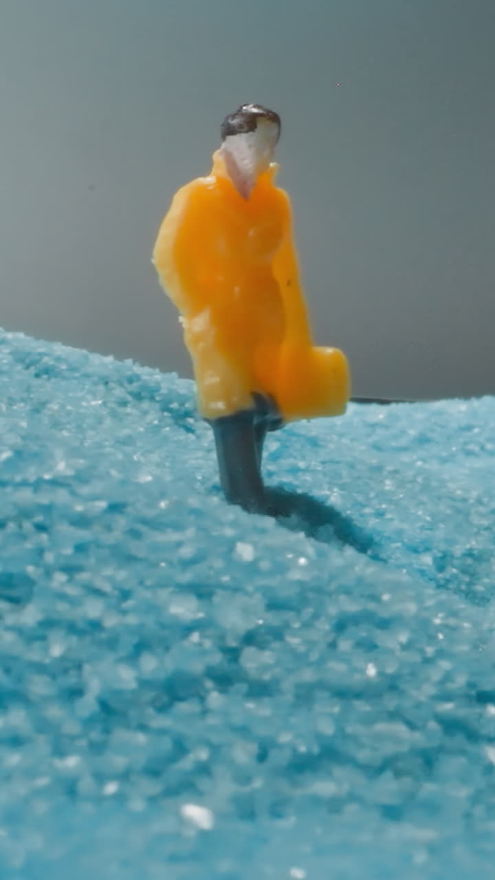 Figure of man with briefcase walking in desert with shimmering blue sand under grey sky. Male person in yellow coat standing near sandy hill macro