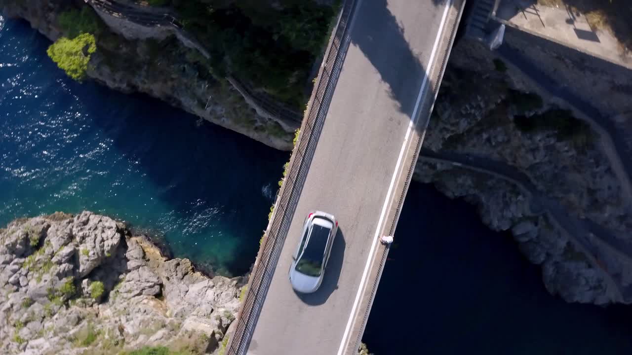 puente de arco fiordo di furore en italia con tráfico de automóviles y un hombre cruzando el tramo, tiro giratorio de la vista superior del dron aéreo