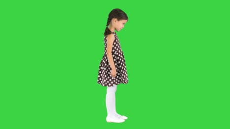 shy little girl in polka dot dress waving her hands around and talking on a green screen, chroma key