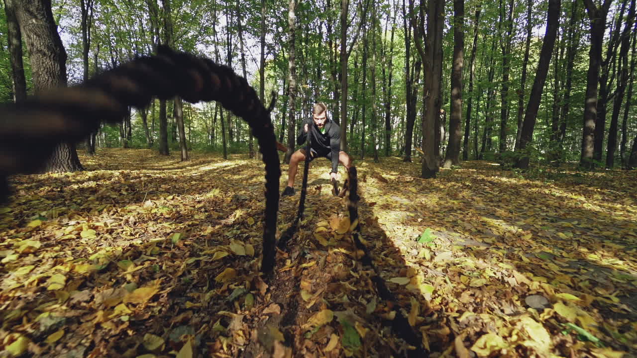 Active man engaged with sporty rope in nature. Sportsman conducts training with the ropes in the autumn forest. Slow motion.