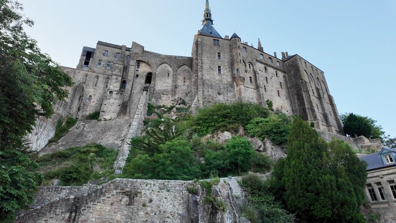 Vista grandangolare della maestosa Abbazia di Mont Saint-Michel dal lato, che evidenzia la sua imponente fortezza medievale, le mura del monastero e la posizione elevata sopra il paesaggio