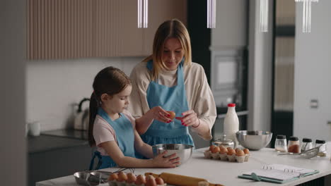 La-Mujer-Y-Su-Pequeña-Hija-Están-Cocinando-Panqueques-En-La-Cocina-De-Casa.-La-Madre-Está-Rompiendo-El-Huevo-En-Un-Tazón.