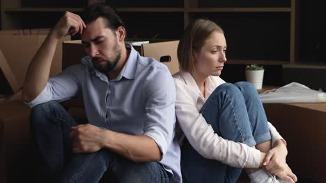 exhausted spouses rest on floor near heap of cardboard boxes