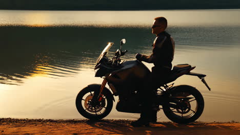 motorcyclist silhouetted by a lake at sunset
