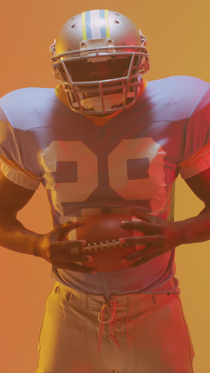 Video verticale di un giocatore di football americano afroamericano con illuminazione arancione neon.