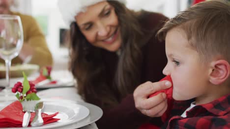 Glückliche-Kaukasische-Mutter,-Die-Ihrem-Sohn-Am-Weihnachtstisch-Den-Mund-Abwischt