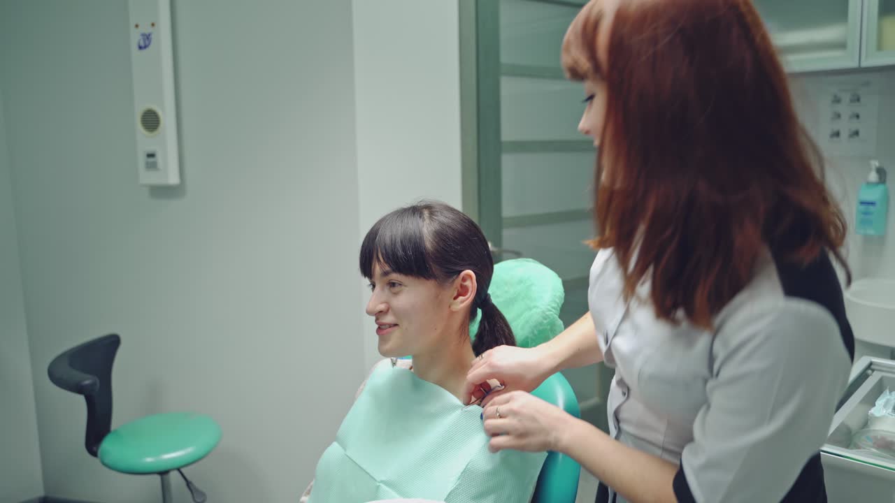 Dentist prepares the smiling patient for teeth treatment on the background of stomatology cabinet. The doctor and young woman in a dentist chair