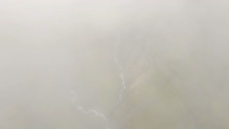 Clouds-parting-revealing-tall-waterfall-and-green-canyon-in-Icelands-Mulagljufur-Canyon