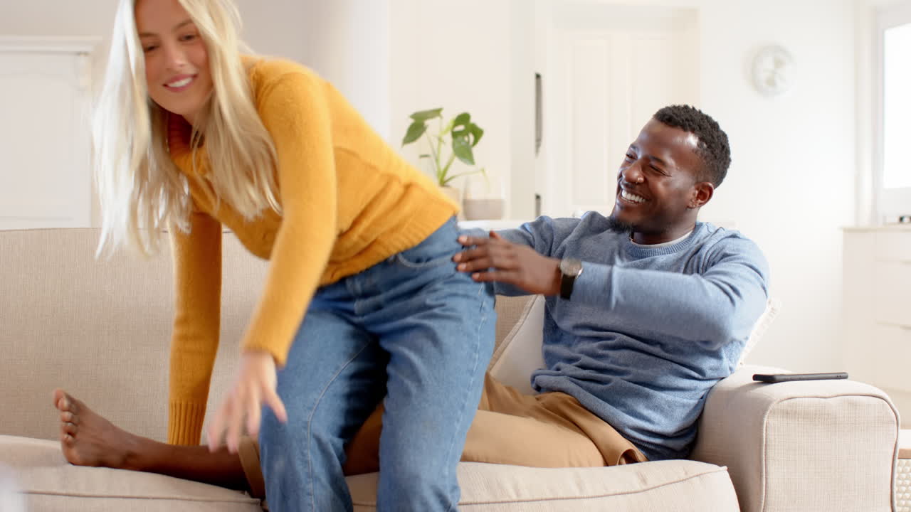 diverse couple laughing together on cozy couch at home, enjoying holiday time, copy space