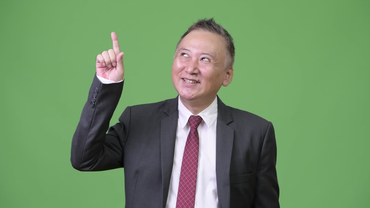 성숙하고 행복한 일본인 사업가가 손가락을 높이 가리키며 생각하고 있다.