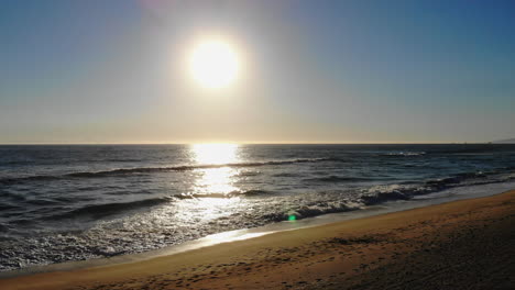 pull back from beautiful ocean sunset past lifeguard tower to empty volleyball courts and huntington beach, california with aerial 4k drone