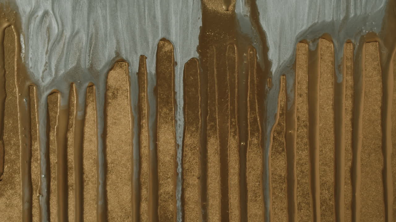 Metallic Silver Paint Dripping Slowly on Textured Gold Surface