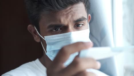 person checking their temperature with a thermometer while wearing a mask