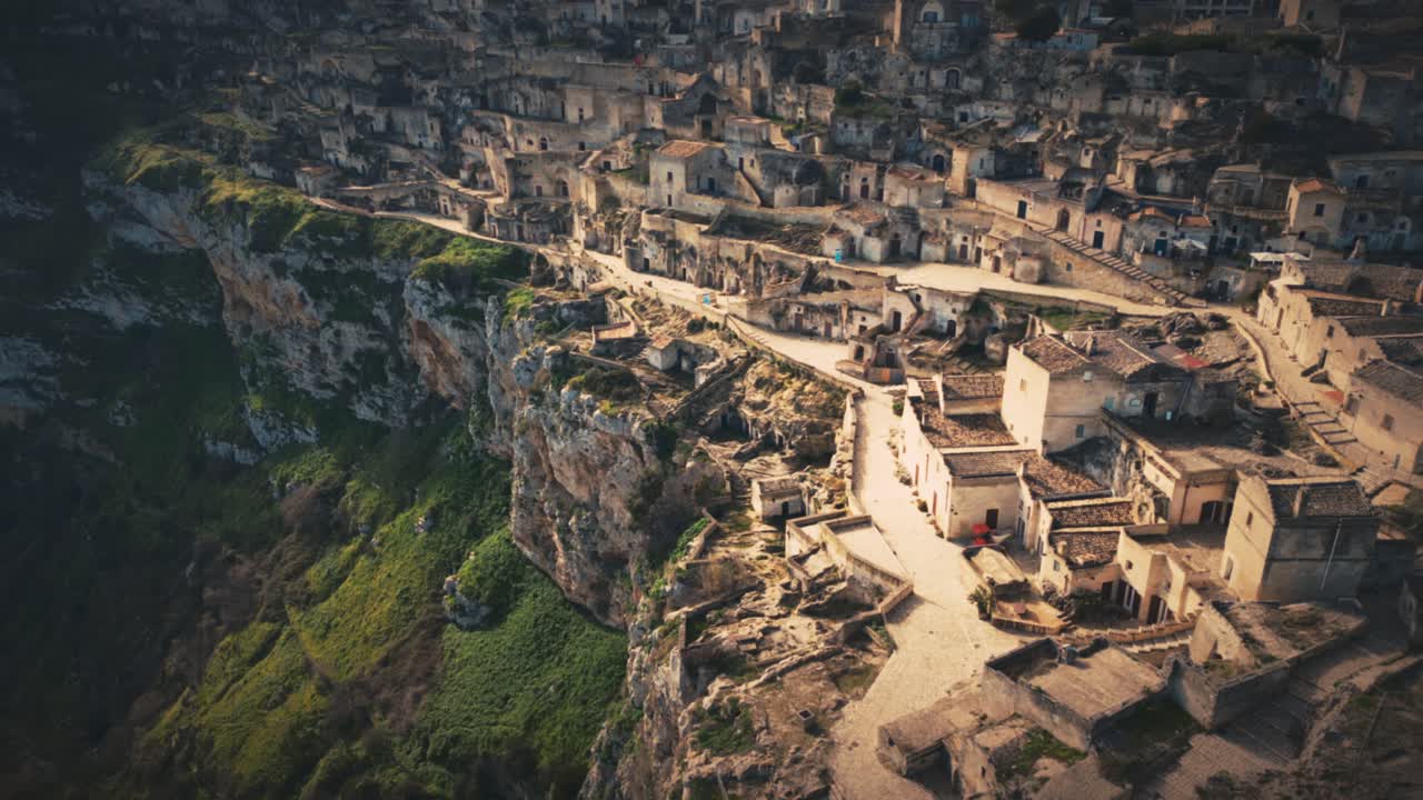 a drone shot of sassi di matera in italy during day with beautiful colours . A cliff on which some of the residential area was built is visible