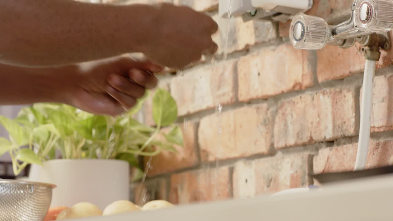 Uomo afroamericano che si sciacqua le mani sotto il rubinetto aperto al lavello della cucina, prendendo un uovo per cucinare.