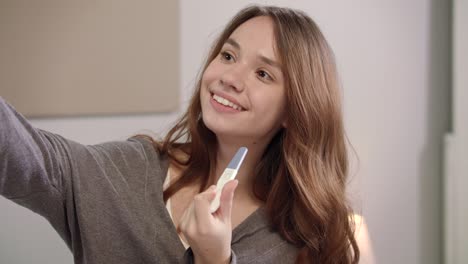 mujer feliz tomando una foto selfie con una prueba de embarazo en el teléfono móvil en el dormitorio