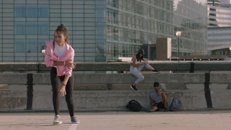 Mujer-Bailando-Joven-Bailarina-De-Hip-Hop-En-La-Ciudad-Realizando-Movimientos-De-Estilo-Libre-Amigos-Multiétnicos-Mirando-Disfrutando-De-La-Práctica-De-Danza-Urbana-Saludando-Emocionado-Sonriendo-Feliz