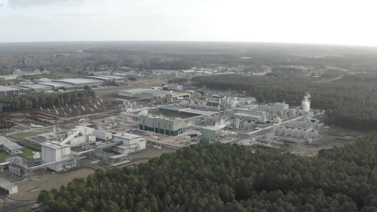 Wide aerial establishing shot of large factory buildings and infrastructure surrounded by forest, industrial production site, Castets, France