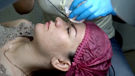 un esteticista profesional hace una corrección de la línea de la ceja a la chica en el salón de belleza y aplica pintura negra con una aguja. 4k. 25 fps.