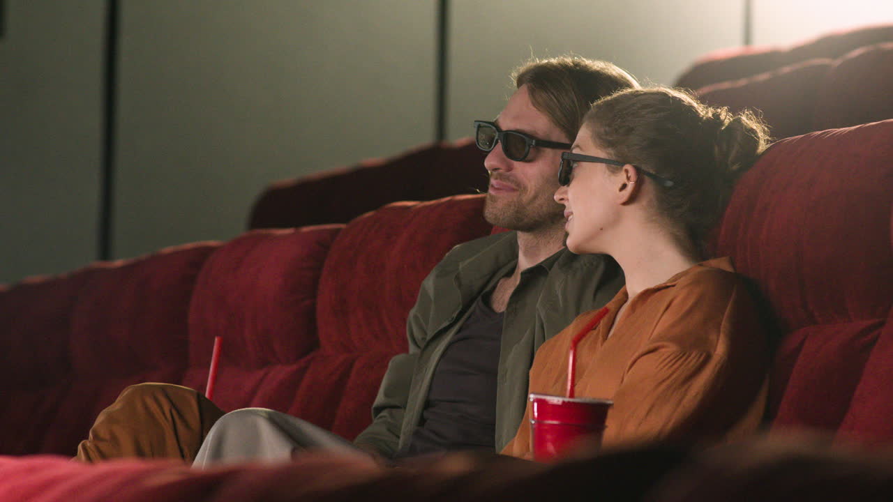 vista lateral de una pareja con gafas 3d sentada en el cine mientras hablan y ven una película 1