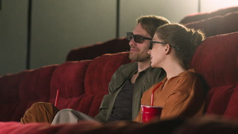 vista lateral de una pareja con gafas 3d sentada en el cine mientras hablan y ven una película 1