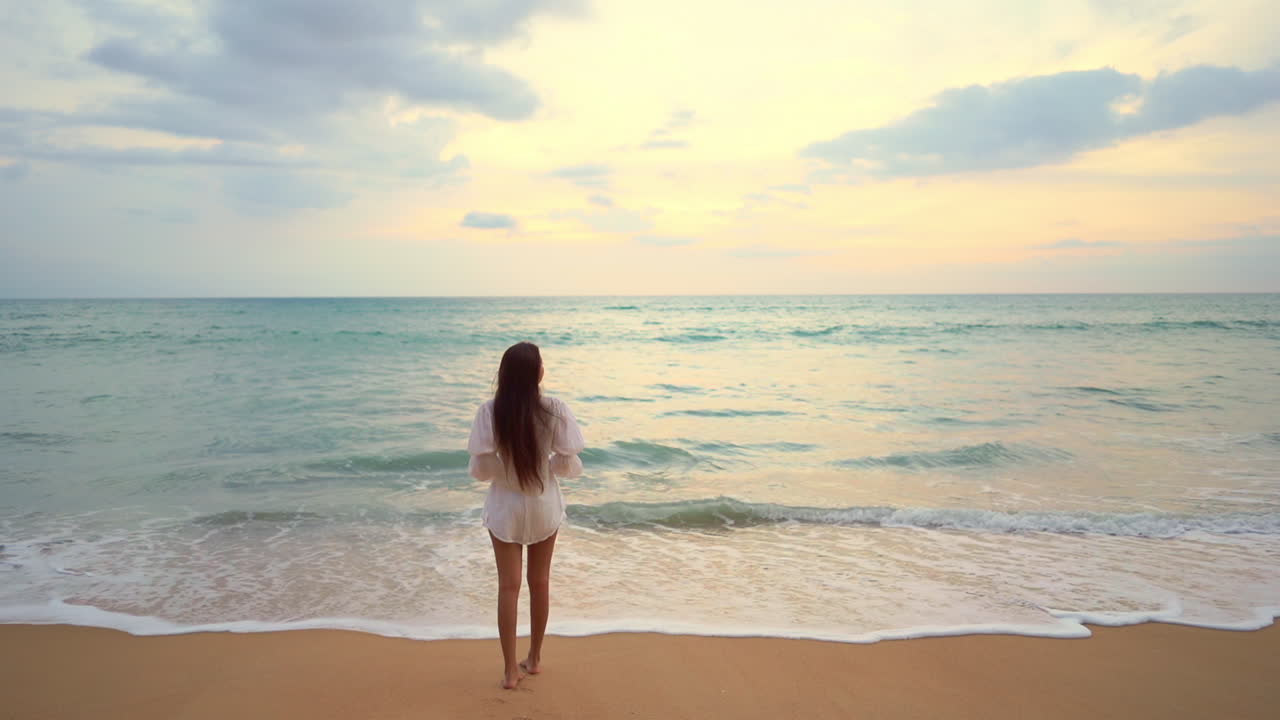 예쁜 젊은 여성이 들어오는 파도를 마주한 해변에 서 있다