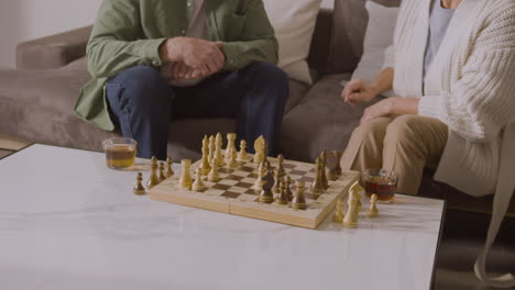 senior man and woman playing chess while sitting on sofa at home 2