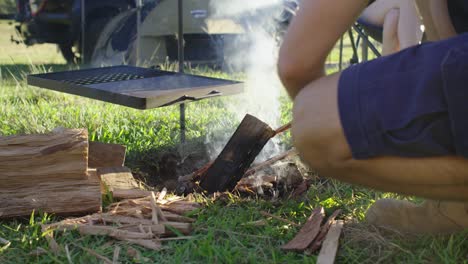 colocar madera en una barbacoa de fogata abierta en un campamento con carpa y vehículo en el fondo
