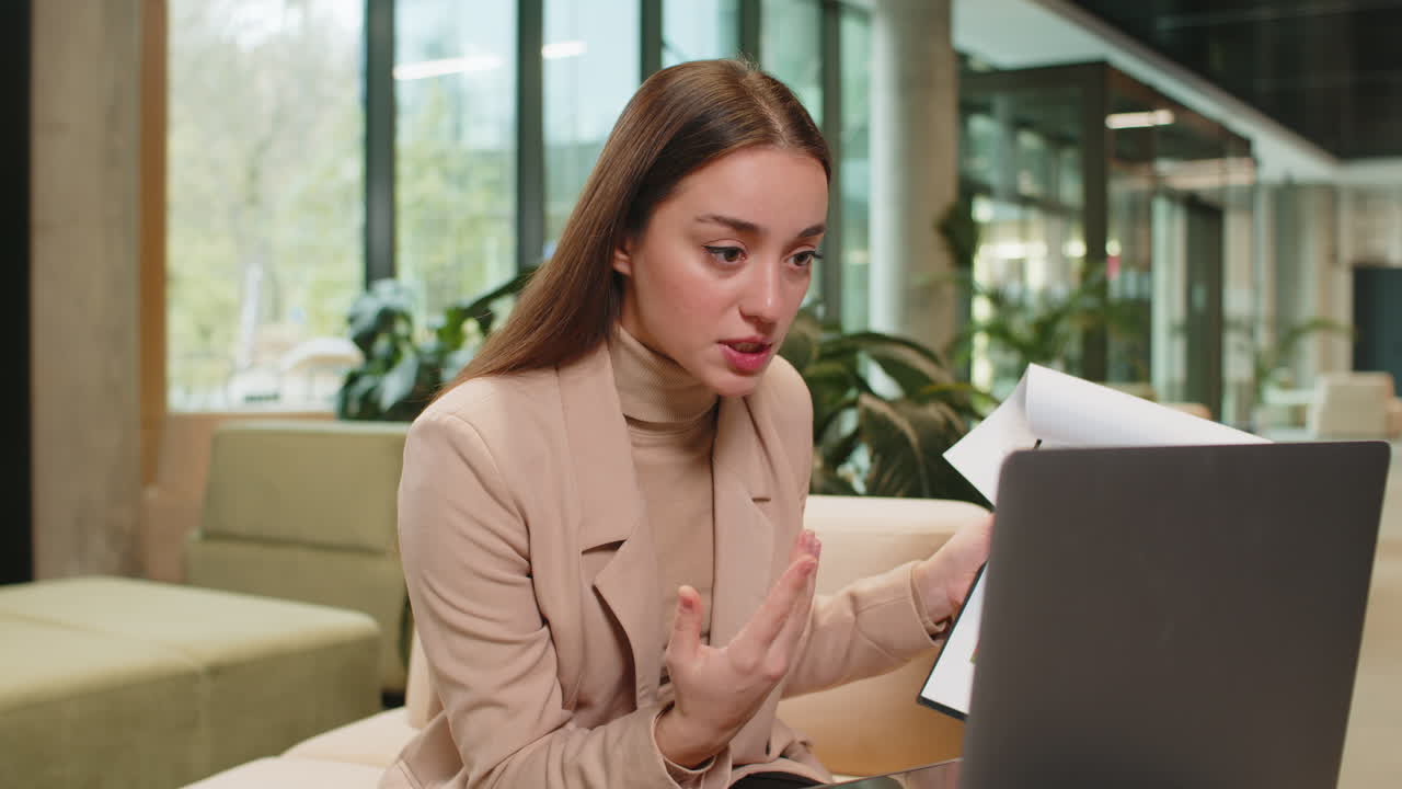 Angry young woman boss arguing over video call in office showing diagram charts reports on laptop