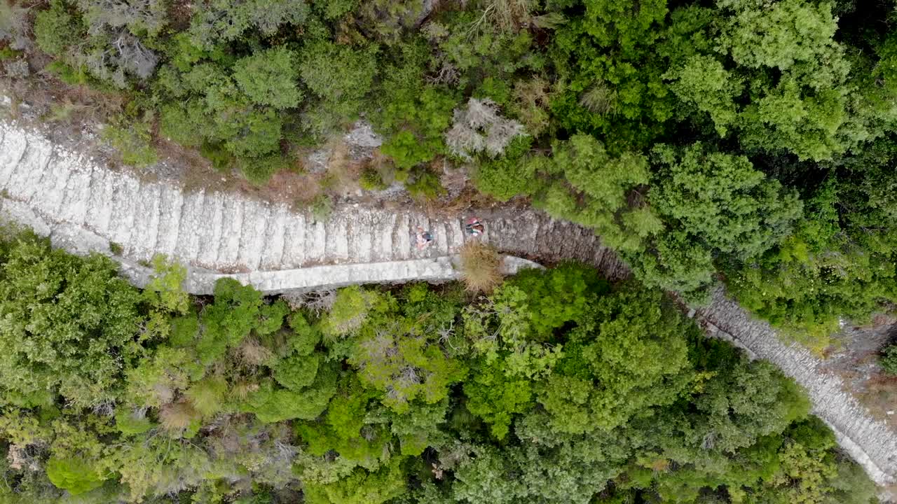 dos personas están caminando a lo largo de un camino costero empinado que corre por la montaña