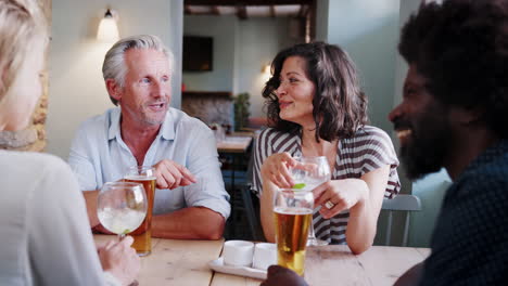 a multi-ethnic group of friends sitting at table in a pub talking and laughing together , close up, over shoulder view